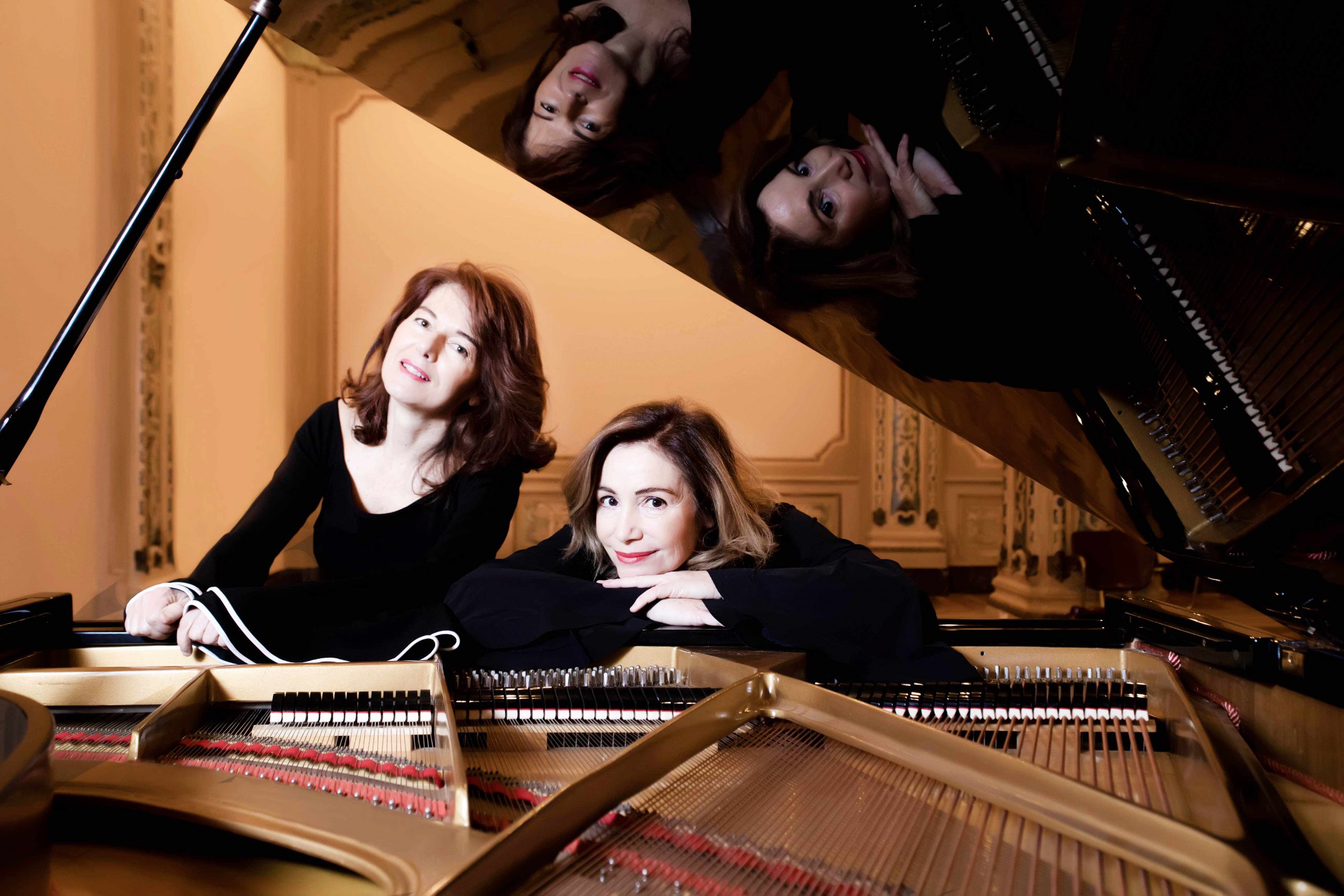 Paola Biondi e Debora Brunialti appoggiate al pianoforte a coda, con riflesso nel coperchio